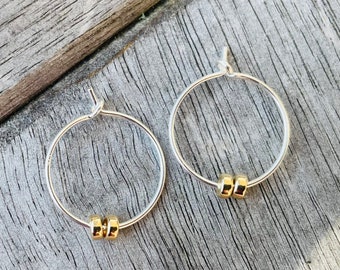 May include: A pair of silver hoop earrings with a small gold bead accent on each hoop.