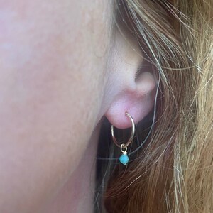 Puede incluir: Aretes de aro de oro con una pequeña piedra turquesa que cuelga de la parte inferior.