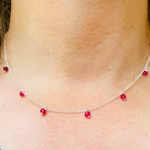 Op de afbeelding: Een zilveren ketting met vijf rode edelsteen kralen die eraan hangen.
