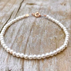 May include: A white pearl bracelet with a rose gold clasp.
