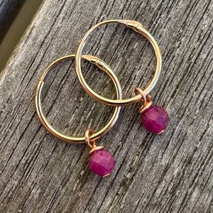 Peut inclure: Boucles d'oreilles créoles en or avec une petite pierre précieuse rose facetée suspendue à chaque créole.