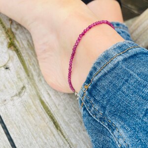 以下が含まれることがあります： 銀色の留め具が付いたピンクの宝石のアンクレット。アンクレットは小さな丸いビーズで作られています。