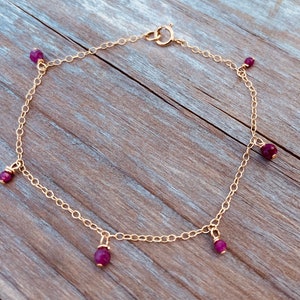 May include: A gold chain anklet with five dangling ruby red gemstones.