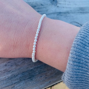 Puede incluir: Un brazalete de perlas blancas con pequeñas perlas espaciadas uniformemente.