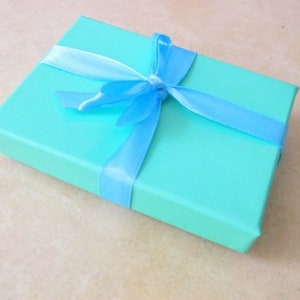 K&ouml;nnte beinhalten: Eine hellblaue Geschenkbox mit einem blauen Band, das zu einer Schleife gebunden ist.