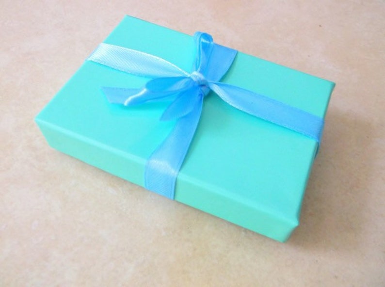 K&ouml;nnte beinhalten: Eine hellblaue Geschenkbox mit einem blauen Band, das zu einer Schleife gebunden ist.