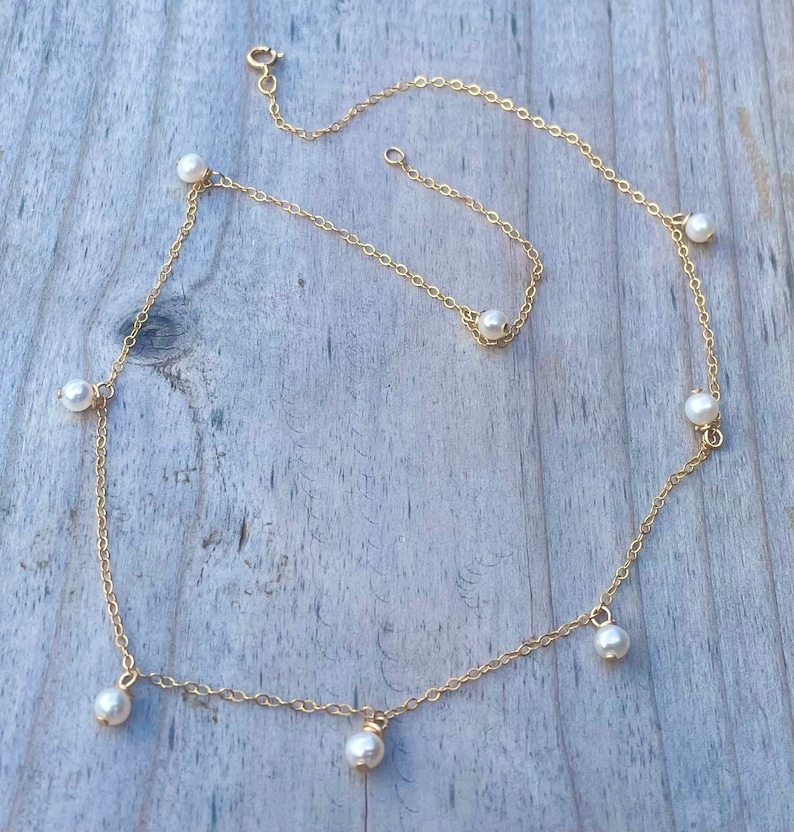 K&ouml;nnte beinhalten: Eine goldene Kettenkette mit mehreren wei&szlig;en Perlenakzenten. Die Kette hat eine zarte Kette und ist mit kleinen, runden Perlen verziert.