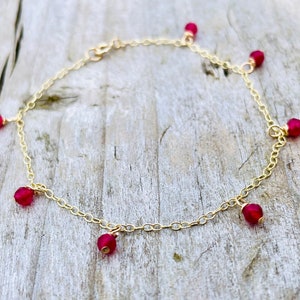 Peut inclure: Un bracelet de cheville en chaîne dorée avec des perles de pierres précieuses rouges pendantes.