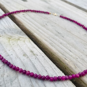 May include: A necklace made of small, faceted, purple gemstone beads. The necklace is on a wooden surface.