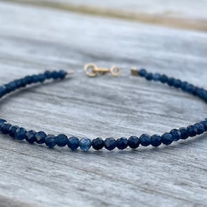 May include: A delicate blue sapphire beaded bracelet with a gold clasp.