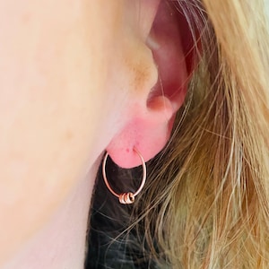 May include: A close-up of a person's ear with a small rose gold hoop earring with a cluster of four smaller hoops hanging from it.