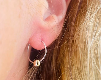 May include: A close-up of a person's ear with a small silver hoop earring with a gold bead accent.