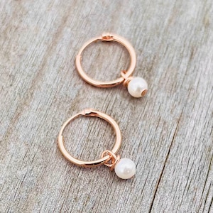 May include: A pair of rose gold hoop earrings with a small white pearl dangling from each hoop.