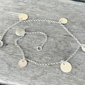 Peut inclure: Un bracelet en chaîne argent avec cinq breloques rondes en argent. Le bracelet a une fermeture à fermoir.