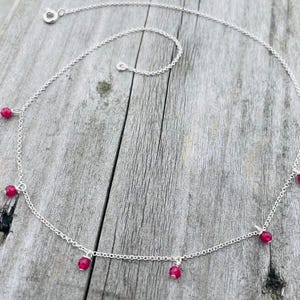 May include: A silver chain necklace with dangling red gemstone beads.