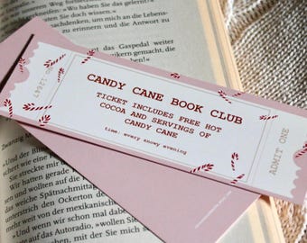 Op de afbeelding: Een roze bladwijzer met een rood-wit ontwerp van een snoepstok. De bladwijzer zegt "Candy Cane Book Club" en "Ticket includes free hot cocoa and servings of candy cane". De bladwijzer zegt ook "Time: every snowy evening" en "Admit One".
