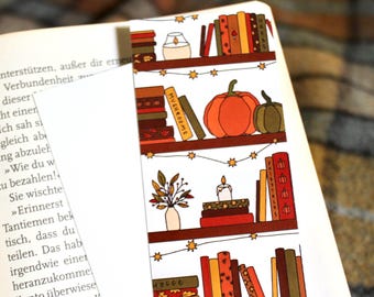 Op de afbeelding: Een witte bladwijzer met een illustratie van een boekenkast. De boekenkast heeft drie planken met boeken, kaarsen, pompoenen en herfstbladeren. De tekst "MUSHROOMS" en "HYGGE" is zichtbaar op de boeken.