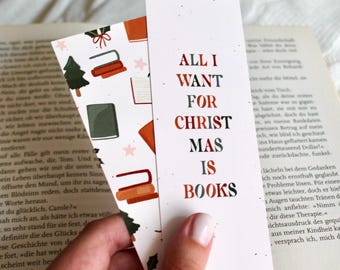 Op de afbeelding: Twee boekenleggers met een boeken thema worden in een hand gehouden. Eén boekenlegger heeft de tekst "ALL I WANT FOR CHRISTMAS IS BOOKS" in rood, zwart en groen. De andere boekenlegger heeft illustraties van boeken en een kerstboom.
