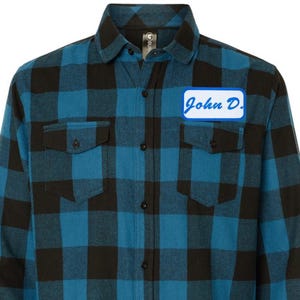 Może przedstawiać: Koszula flanelowa w niebiesko-czarną kratę z niebieską metką z napisem "John D."