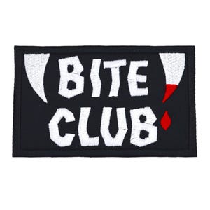May include: A rectangular black patch with the words "BITE CLUB" in white, stylized text. The design includes white fangs and red blood drop accents. The patch is likely for clothing or accessories.