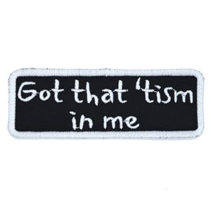 Op de afbeelding: Een rechthoekige zwarte patch met witte geborduurde tekst die luidt: "Got that 'tism in me." De patch heeft een witte rand en is ontworpen om op kleding of accessoires te worden genaaid of gestreken.