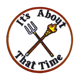 Op de afbeelding: Geborduurde patch met een witte achtergrond en een bruine rand. De patch heeft een gekruist hooivork- en fakkelontwerp. De tekst "It's About That Time" is in een boog rond het ontwerp in zwart.