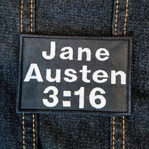 Peut inclure: Écusson en tissu noir avec du texte blanc qui dit "Jane Austen 3:16".