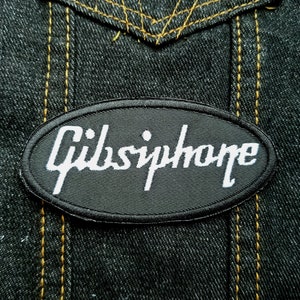May include: Black oval patch with white embroidered text that reads "Gibson" on a denim background.