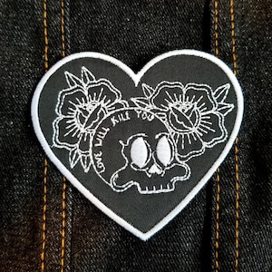 May include: Black and white embroidered patch in the shape of a heart. The heart features a skull with the words "Love Will Kill You" around it. Two white flowers are on either side of the skull.