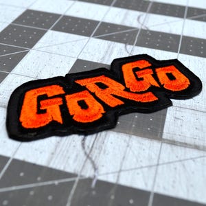 Close up detail of an orange and black embroidered logo patch for the classic Kaiju monster movie Gorgo.