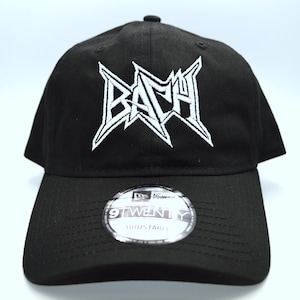 Può includere: Cappellino da baseball nero con un logo ricamato bianco che dice "BACH" in un font stilizzato. Il cappellino ha un cinturino regolabile nero con un logo New Era.