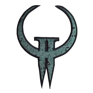 May include: A patch featuring the iconic Quake logo. The design is a teal and black emblem with a distinctive shape, including a curved top and a stylized central element. The patch has a textured appearance.