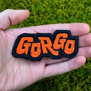 Orange and black embroidered logo patch for the classic Kaiju monster movie Gorgo. Shown in the palm of a hand for size reference.