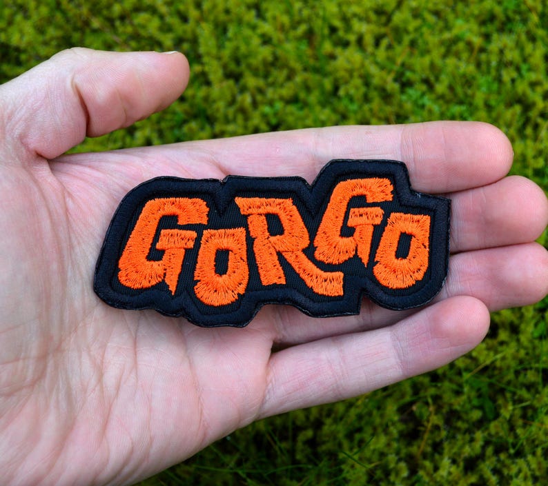 Orange and black embroidered logo patch for the classic Kaiju monster movie Gorgo. Shown in the palm of a hand for size reference.