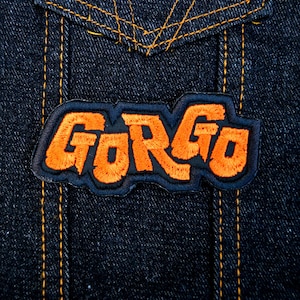 Orange and black embroidered logo patch for the classic Kaiju monster movie Gorgo. Shown on a denim jacket.