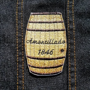 May include: A brown and gold embroidered patch of a wooden barrel with the text "Amontillado 1846" on it.