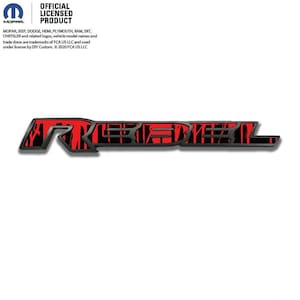 May include: A black and red "REBEL" emblem. The word "REBEL" is in a bold, stylized font with a red and black pattern. The emblem has a slight shadow effect, giving it a three-dimensional appearance. The official licensed product logo is in the upper left corner.