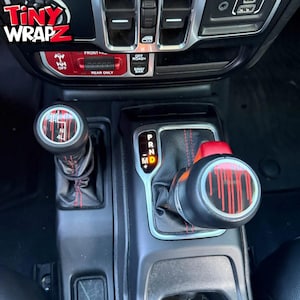 May include: Interior view of a vehicle's console featuring custom shift knobs and control panel accents. The shift knobs have a black base with red and white graphic designs. The control panel is red with white lettering.