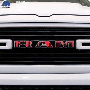Può includere: Una griglia anteriore di un camion bianca con un emblema RAM nero caratterizzato da un motivo a goccia rosso. Il logo Mopar e il testo OFFICIAL LICENSED PRODUCT sono visibili nell'angolo in alto a sinistra sul cofano bianco.