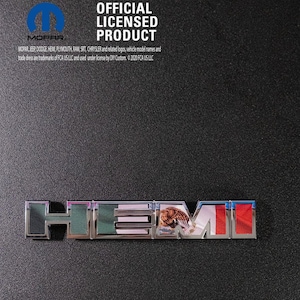 May include: A chrome "HEMI" emblem with a tiger graphic, set against a black background. The emblem is an official licensed product, with the MOPAR logo visible. The text "OFFICIAL LICENSED PRODUCT" is also displayed.