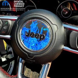 May include: Black steering wheel with a silver Jeep logo and a blue flame design. The steering wheel is part of a car's interior, with red stitching visible. The image also includes the text "OFFICIAL LICENSED PRODUCT".
