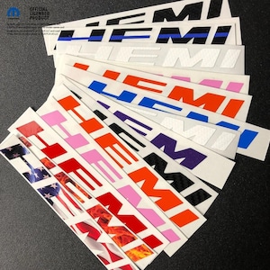 May include: A collection of "HEMI" decals in various colors, including red, pink, orange, purple, and black. Some decals feature American flag and flame designs. The decals are rectangular and have a glossy finish.