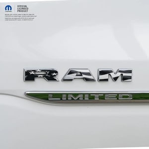 May include: Chrome RAM emblem with a flag design on a white vehicle. The word "RAM" is displayed in chrome, with the "R" featuring a star pattern and the "A" and "M" having a striped design. Below, a green "LIMITED" emblem is visible.