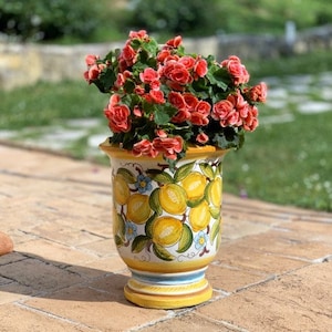 Könnte beinhalten: Ein weißer Keramiktopf mit einem gelben und grünen Zitronenmuster. Der Topf ist mit rosa Blumen gefüllt.
