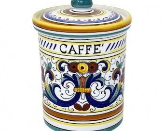 Op de afbeelding: Een witte keramische koffiebus met een blauw en geel bloemenmotief. Het deksel heeft een groene knop en de bus heeft de tekst "CAFFE" in bruine letters.