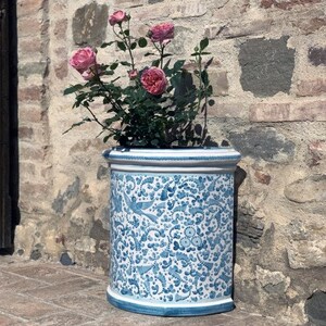 May include: A white ceramic planter with a blue and white floral design. The planter is filled with a pink rose bush.