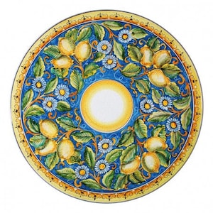 May include: A large, round ceramic plate with a blue background and a yellow border. The plate is decorated with a floral pattern of lemons, leaves, and flowers. The centre of the plate features a yellow sun with a white centre.