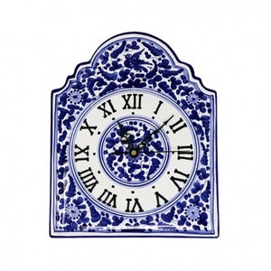 May include: A decorative wall clock with a white face and Roman numerals. The clock is framed in a blue and white floral design. The clock hands are black. The clock is approximately 12 inches tall and 9 inches wide.
