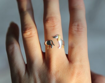 May include: A silver ring featuring two dachshund dogs, one standing and one sitting, with a gold accent on the standing dog.