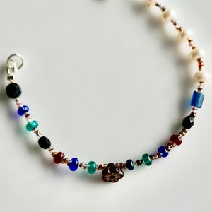 May include: A multi-colored beaded bracelet with a silver clasp. The bracelet features black, white, blue, green, and red beads, as well as a brown flower charm.